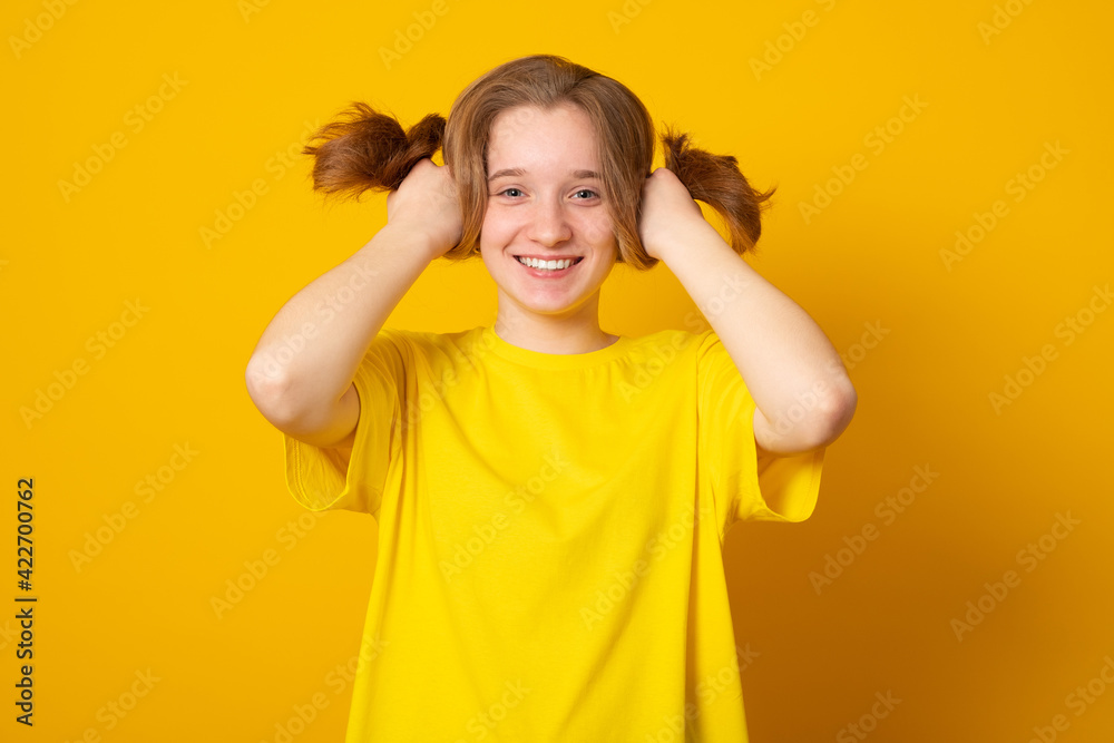 Funny girl with a two-ponytail hairstyle smiles grimaces and laughs on a yellow background. Funny girl with a two-ponytail hairstyle smiles grimaces and laughs on a yellow background.