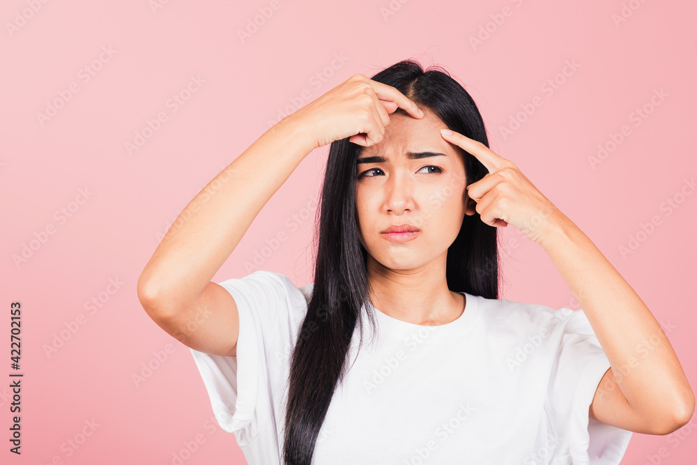 Portrait teenage Asian beautiful young woman having skin problems squeezing pimples on her face, studio shot on pink background, with copy space, Thai female acne, beauty care concept Portrait teenage Asian beautiful young woman having skin problems squeezing pimples on her face, studio shot on pink background, with copy space, Thai female acne, beauty care concept