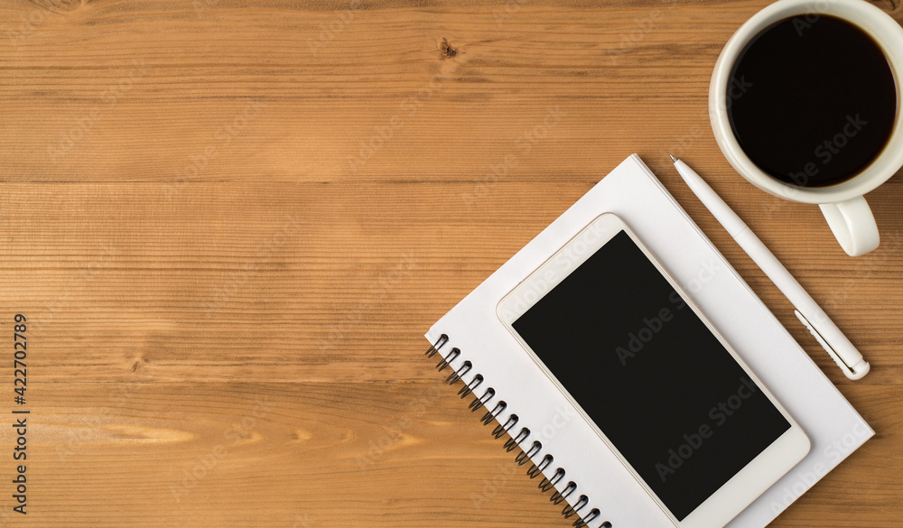 Top view photo of workplace with pen white cup of coffee and smartphone display on copybook isolated wooden table background with copyspace Top view photo of workplace with pen white cup of coffee and smartphone display on copybook isolated wooden table background with copyspace