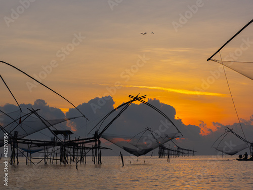 Silhouette photo of fisherman trap fish in front of sunrise scene at famous Pak Pra Phatthalung provience Thailand photo