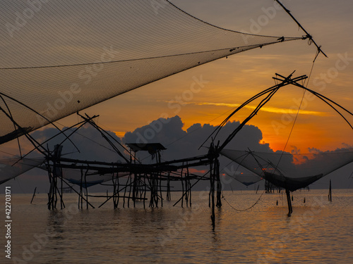 Silhouette photo of fisherman trap fish in front of sunrise scene at famous Pak Pra Phatthalung provience Thailand photo