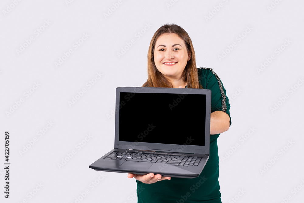 Smiling young plump girl in fashion dress posing isolated on gray background. People lifestyle concept. Mock up copy space laptop. Hold pc computer with blank empty screen, winner plus size woman Smiling young plump girl in fashion dress posing isolated on gray background. People lifestyle concept. Mock up copy space laptop. Hold pc computer with blank empty screen, winner plus size woman
