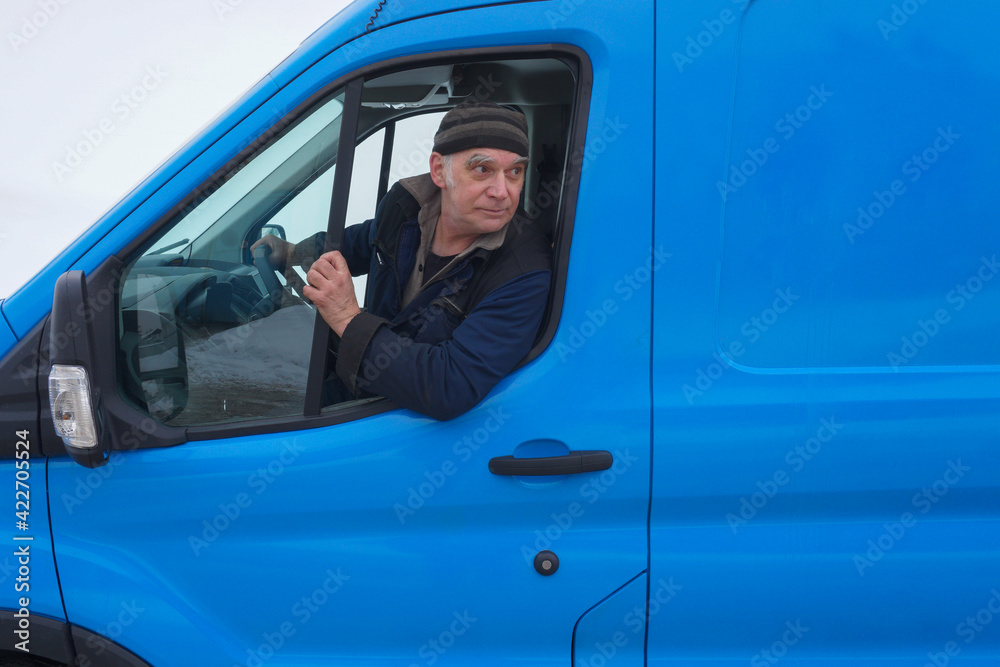 An elderly driver, sitting in a car behind the wheel, looks back through an open window. An elderly driver, sitting in a car behind the wheel, looks back through an open window.