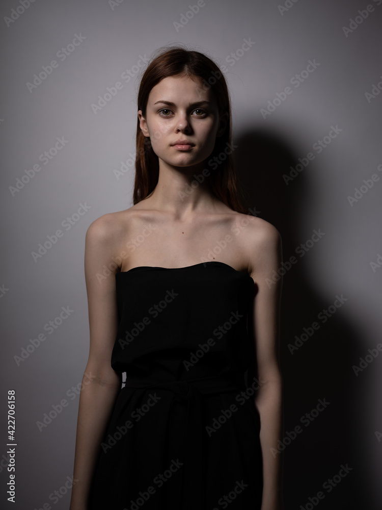 Naklejka premium Beautiful woman with red hair in a black dress on a gray background bared shoulders