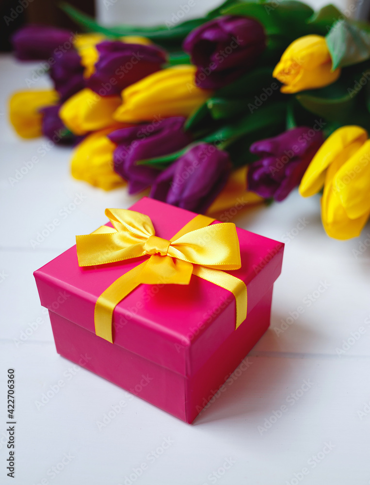pink gift box with yellow bow on the background of a bouquet of tulips pink gift box with yellow bow on the background of a bouquet of tulips
