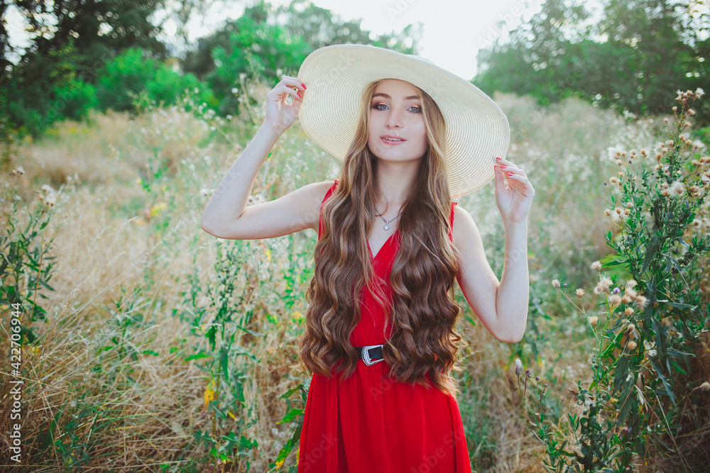 Young beautiful girl in red dress and hat on nature