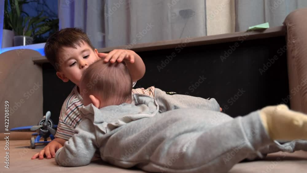 Small caucasian boy is playing with his newborn brother touching his head and smile Small caucasian boy is playing with his newborn brother touching his head and smile