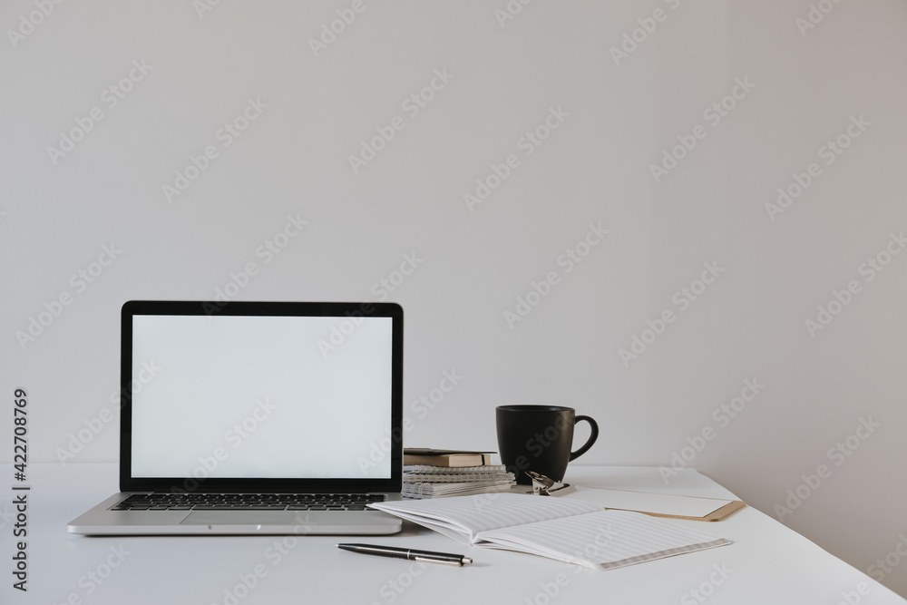 Minimalist home office desk workspace. Laptop with blank copy space mockup on table with coffee cup, paper sheet, stationery against white wall. Work, business background. Minimalist home office desk workspace. Laptop with blank copy space mockup on table with coffee cup, paper sheet, stationery against white wall. Work, business background.