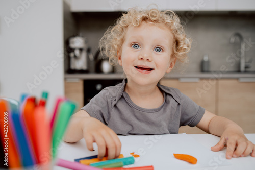 Portrait of smiling pre-school girl sitting at her kitchen table playing with plasticine. The cute lovely girl is spending his afternoon free time at home.