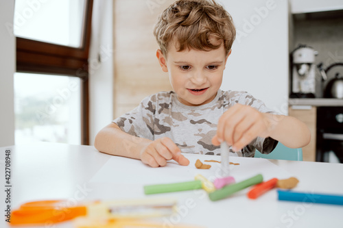 Portrait of a School-aged Boy sitting at kitchen table playing with plasticine. The boy is spending his afternoon free time at home.
