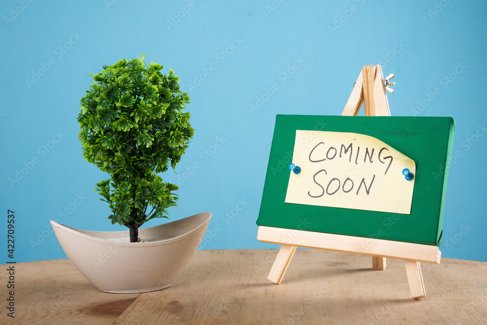 coming soon written on a sticky note on a mini green notice board with ...