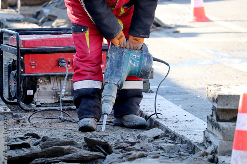 Worker repair the road surface with a jackhammer. Construction work, laying of paving slabs in city
