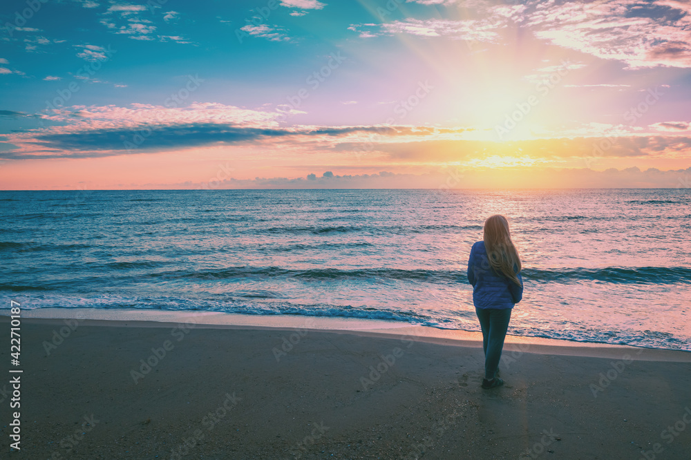 Seascape at sunrise with beautiful sky. Woman on the beach during sunrise. Young happy woman stands on the beach and looks at the sunrise Seascape at sunrise with beautiful sky. Woman on the beach during sunrise. Young happy woman stands on the beach and looks at the sunrise