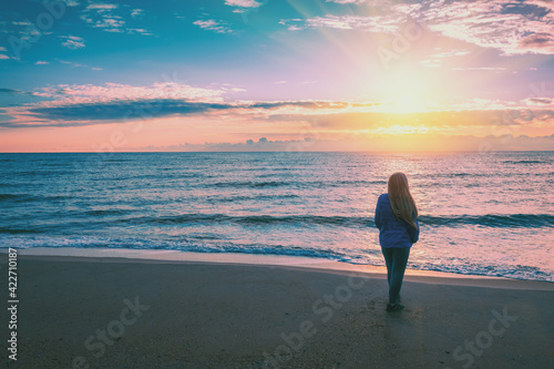 Seascape at sunrise with beautiful sky. Woman on the beach during sunrise. Young happy woman stands on the beach and looks at the sunrise