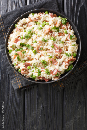 Venetian food Risi e Bisi of rice with peas and ham slices close-up in a plate on the table. horizontal top view above