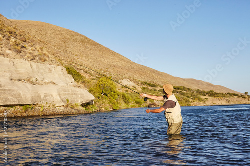 Angler fishing in a river in Patagonia with mountain in the background.