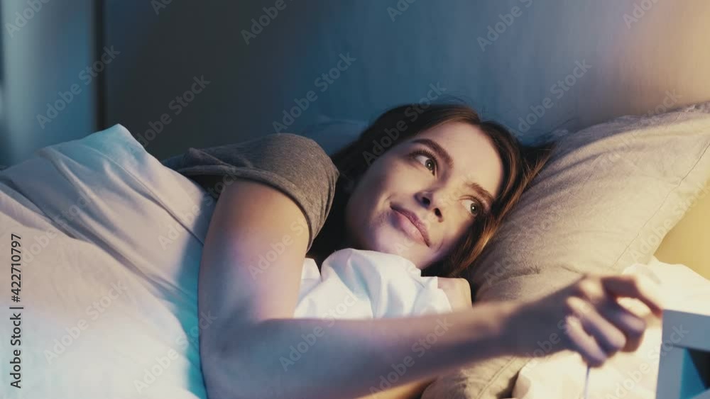 Good night. Sweet dreams. Bedtime rest recreation. Happy relaxed satisfied woman lying down in cozy comfortable bed turning off light falling asleep smiling in dark bedroom with blue moonlight.