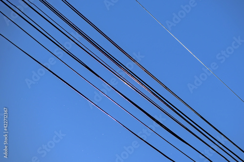 Electric wires illuminated by sunlight on one side against the blue sky
