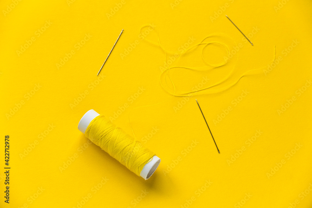 Yellow thread reel with a needle on yellow background