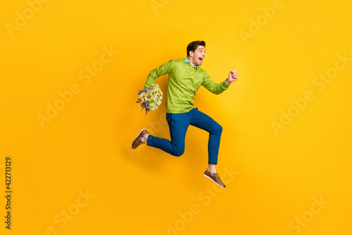 Full length body size profile side view of nice cheerful guy jumping running bringing flowers floral isolated on vivid yellow color background