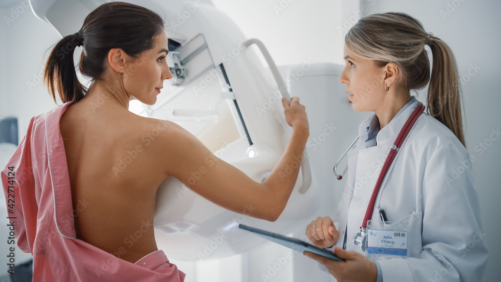 Obraz premium Friendly Female Doctor Explains the Mammogram Procedure to a Topless Adult Female Patient Undergoing Mammography Scan. Healthy Woman Does Cancer Prevention Routine in Hospital Room.