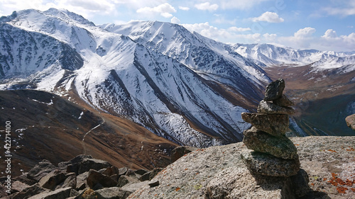 A pile of stones points the way. The stones of the pyramid indicate the direction of tourists. View of snowy mountains, gorges and sky with clouds. Panorama for the desktop.