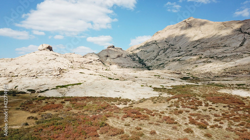 Huge rocks from lava. A former volcano. Bektau-ATA Tract. Large rocks, rifts, cracks, and mountains. In places, grass grows and water is visible. Unusual Martian landscape. Blue sky and clouds.