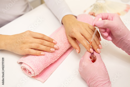 Close-up of a manicurist applying moisturizing nail oil on person's hand. On the photo we see pink towel