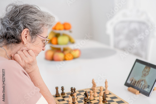 Pensive senior woman uses tablet computer to play chess with her friends during quarantine Coronavirus (Covid-19) epidemic photo