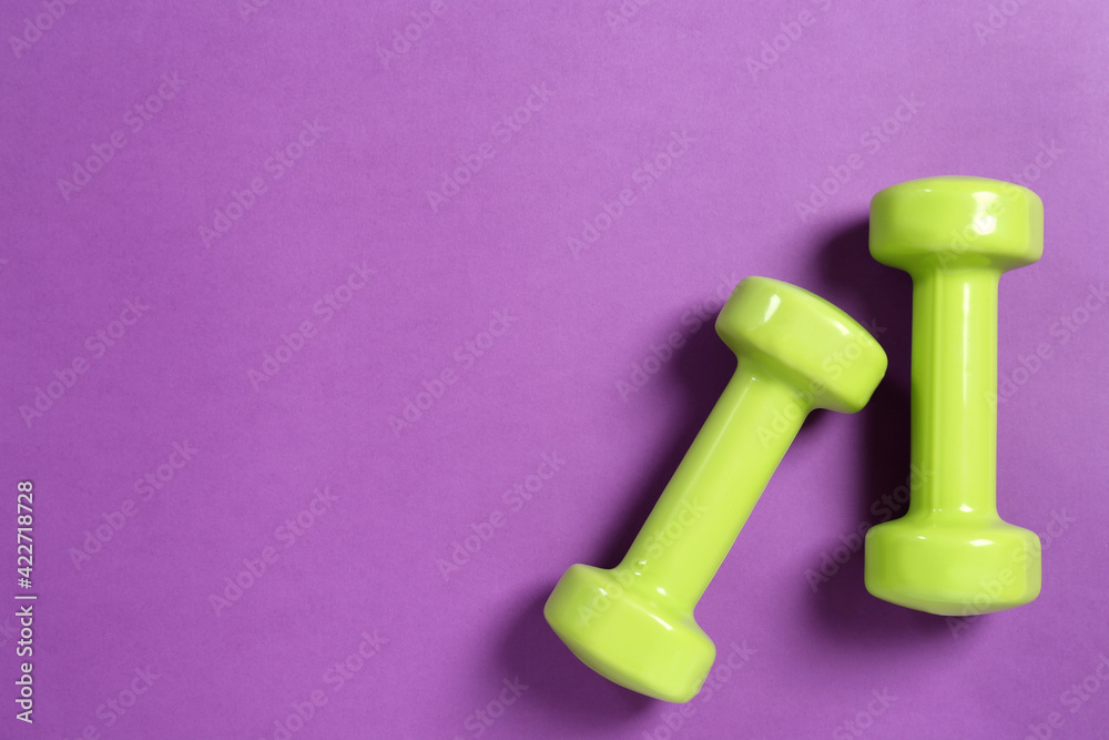 Bright dumbbells on violet background, flat lay. Space for text Bright dumbbells on violet background, flat lay. Space for text
