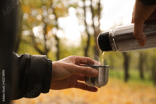 Man pouring drink from thermos into cap outdoors, closeup