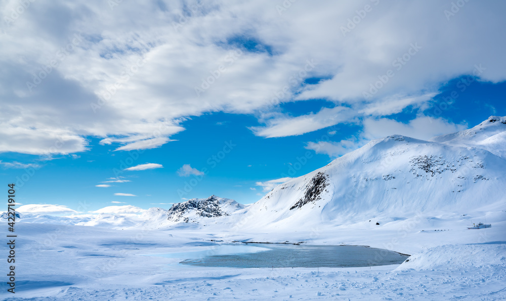 Winter in the mountains with a large lake of water from a melting glacier.