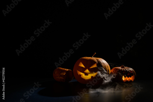 Pumpkins with carved grimaces and candles inside in the dark for halloween. Jack o latern in smoke. photo