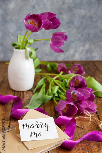 Bouquet of purple tulips and MARRY ME card on wooden table