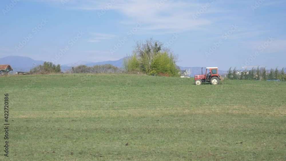 Tractor working on cultivated fields farmland on the mountains, agriculture occupation, lush green cereal crops, sprintime in Italy, native flat color profile Tractor working on cultivated fields farmland on the mountains, agriculture occupation, lush green cereal crops, sprintime in Italy, native flat color profile
