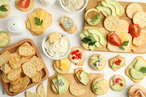 Different snacks with salted crackers on white wooden table, flat lay