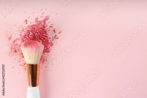 Makeup brush and scattered blush on pink background, top view. Space for text photo