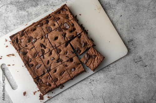 Dark chocolate brownie cut into 16 square pieces. The item is on white plastic cutting board with chocolate crumbs photo