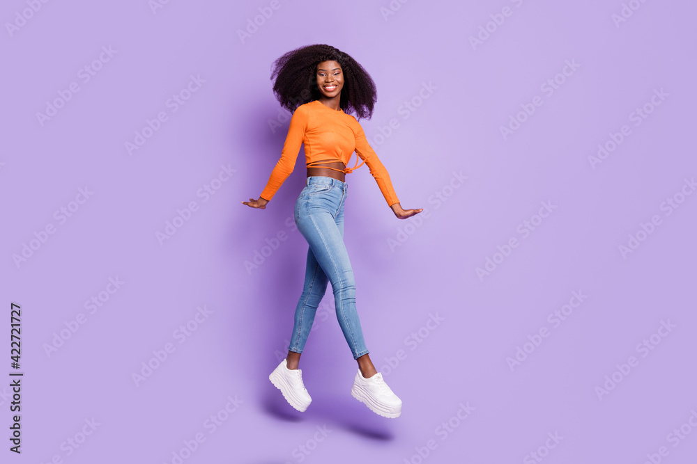 Full size photo of hooray nice brunette lady jump go wear orange top jeans sneakers isolated on lilac background
