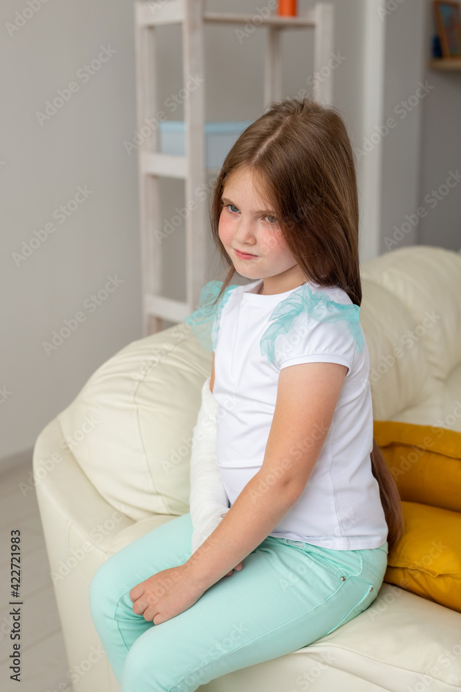 Child with a cast on a broken wrist or arm smiling and having fun on a couch. Positive attitude, recovery and kid concept. Child with a cast on a broken wrist or arm smiling and having fun on a couch. Positive attitude, recovery and kid concept.