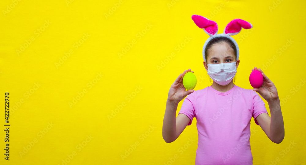 Funny girl in a pink T-shirt and rabbit ears on a yellow background in her hands holds pink and yellow eggs.