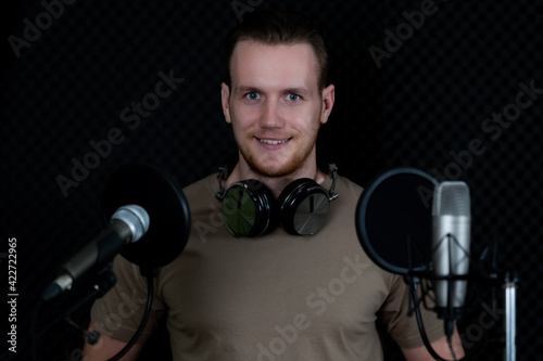 Portrait of young and handsome male singer with microphone and equipment working in voice recording studi