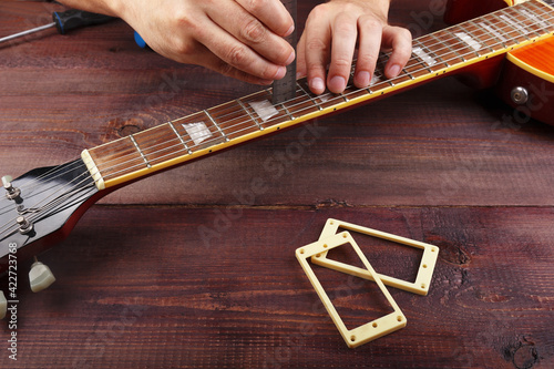 Fotografie Guitar repairman measures the relief of neck on electric guitar at workplace