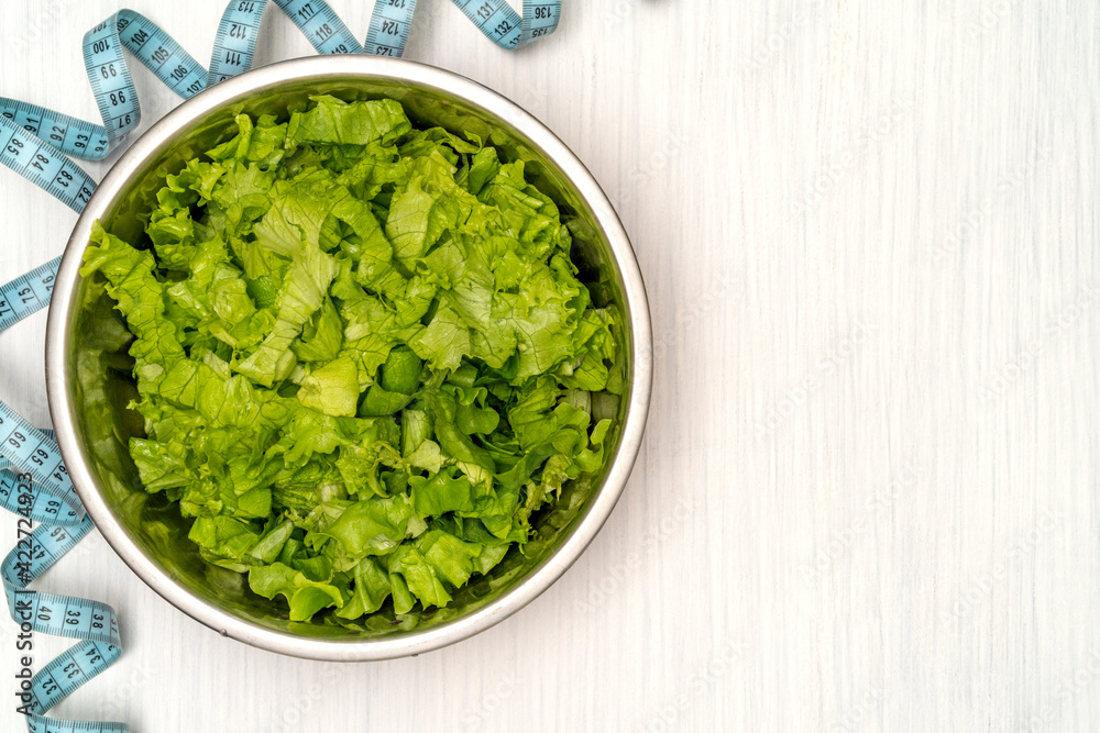 Salad with fitness measuring tape over wooden background Salad with fitness measuring tape over wooden background