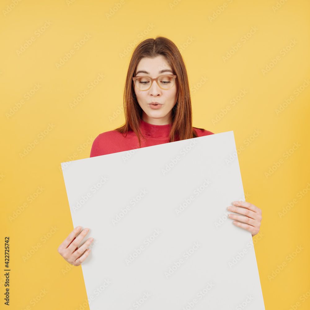 Sceptical young woman looking down at a blank placard she is holding Sceptical young woman looking down at a blank placard she is holding