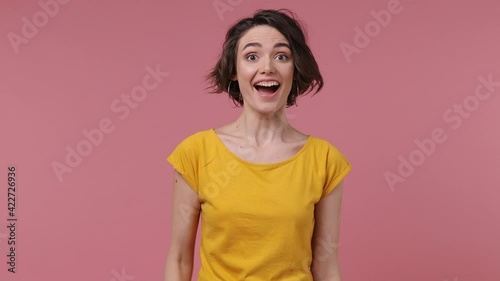 Brunette short hairdo young woman 20s wears basic casual yellow t-shirt look around for friend find waving meet greet with hand as notices someone isolated on pastel pink background studio portrait