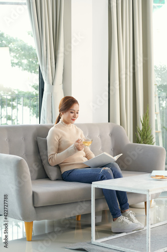 Free Download A picture of nice and thoughtful girl sits at sofa and reads a book. - GFXLoad