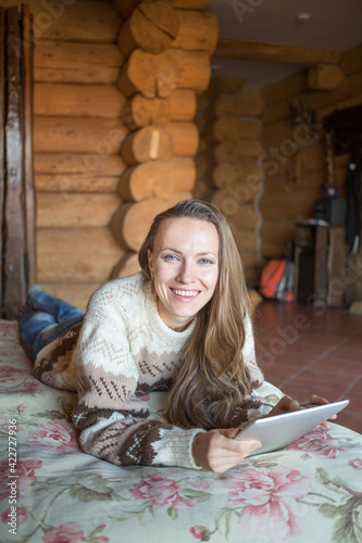 Rural escape. Woman in wooden rural scenery home interior, woman lying on bed with a laptop