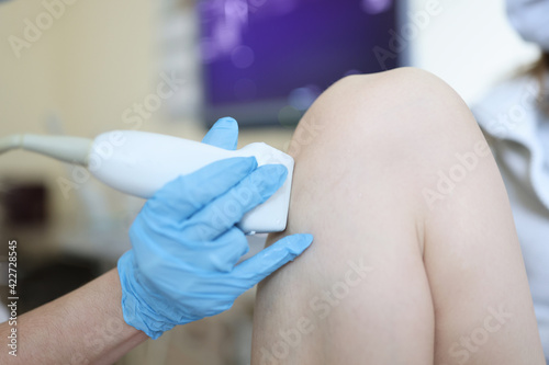 Doctor making ultrasound examination of patient knee joint closeup