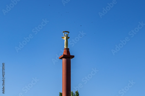 Kherson, Ukraine - July 22, 2020: Top of Victory Monument with a statue of Greek goddess Nike (Kherson) isolated on a blue sky background, close-up. Tall pillar topped with a female figure with wings photo